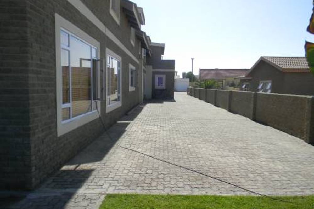 A side view of the guest house featuring paved driveway access, brick exterior walls, and secure perimeter walling.