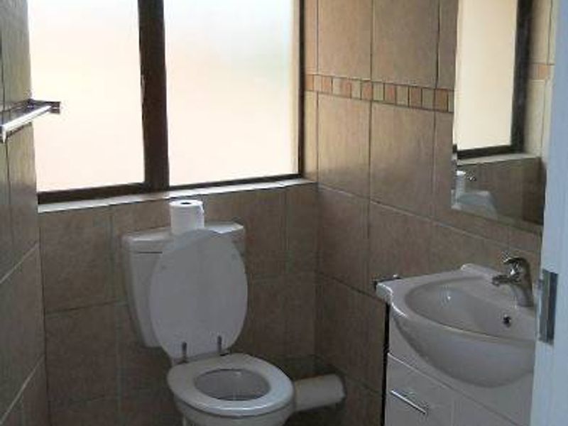 A functional bathroom featuring tiled walls and flooring, a vanity cabinet with a wash basin, and a frosted window for privacy.