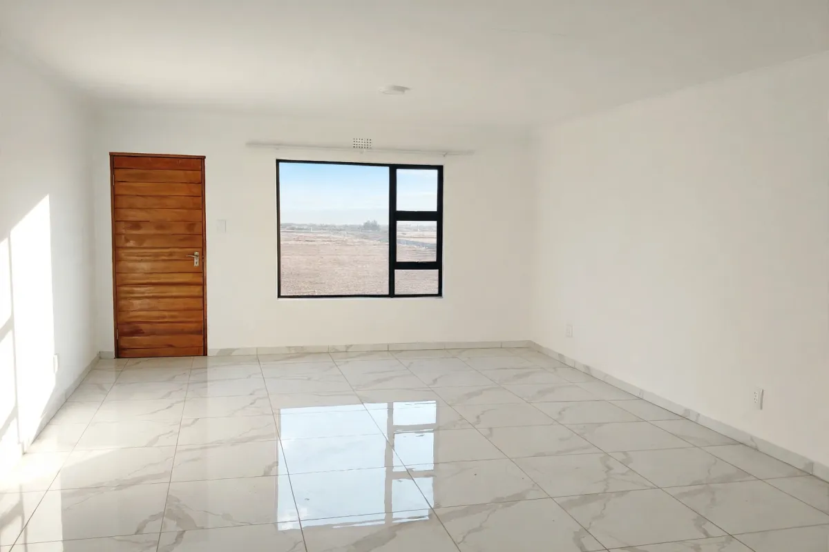 A bright, empty living area featuring polished marble-look floor tiles, a wooden door, and a large window with views of the surrounding landscape.