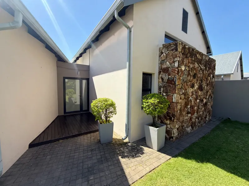 Rear exterior view featuring a stone-clad feature wall, timber decking, and a paved patio area leading to a glass entrance door.
