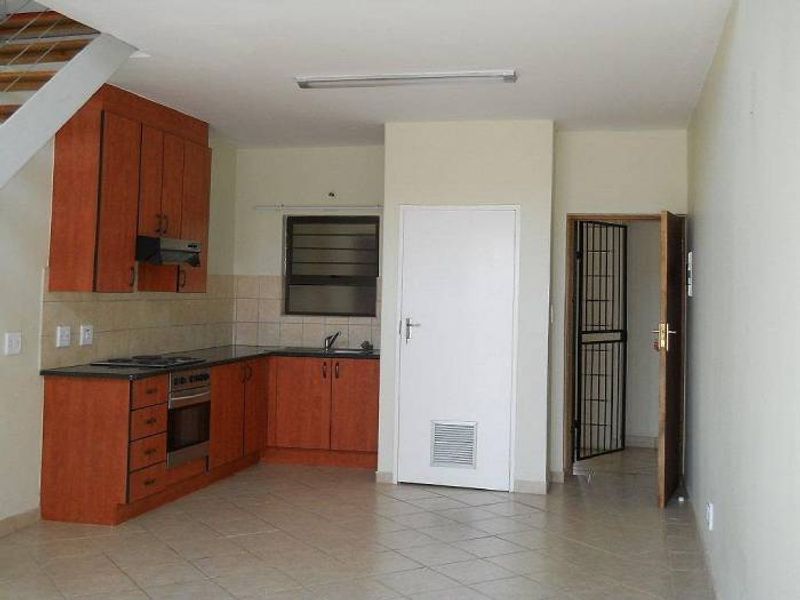 Open plan kitchen area featuring wooden cabinetry, built-in oven and hob, tiled flooring, and direct access to an adjacent room with a security gate.