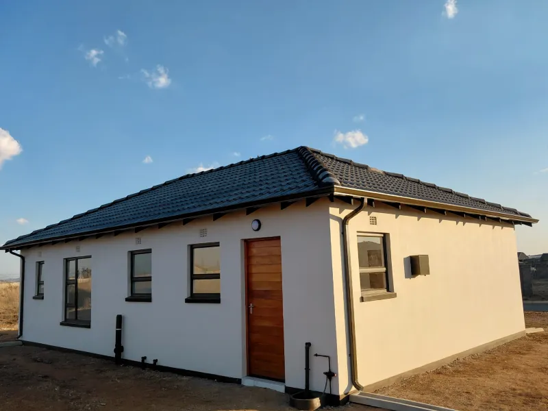 A well-maintained modern house exterior featuring a tiled roof, clean white rendered walls, timber door, and aluminium window frames.