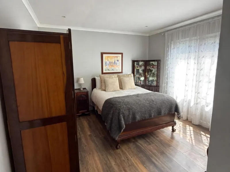 A well-maintained bedroom featuring wood-look laminate flooring, recessed downlighting, and neutral wall finishes with natural light from the window.