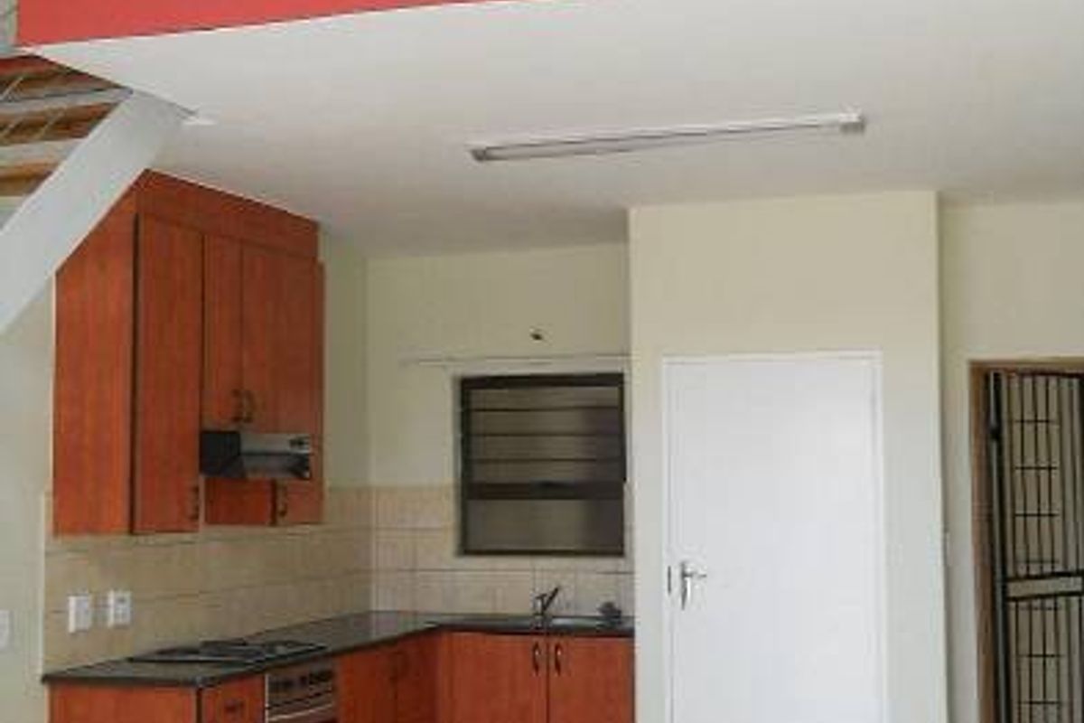 Open-plan kitchen area featuring wooden cabinetry, built-in appliances, and tiled flooring, with an adjacent mezzanine level and staircase.