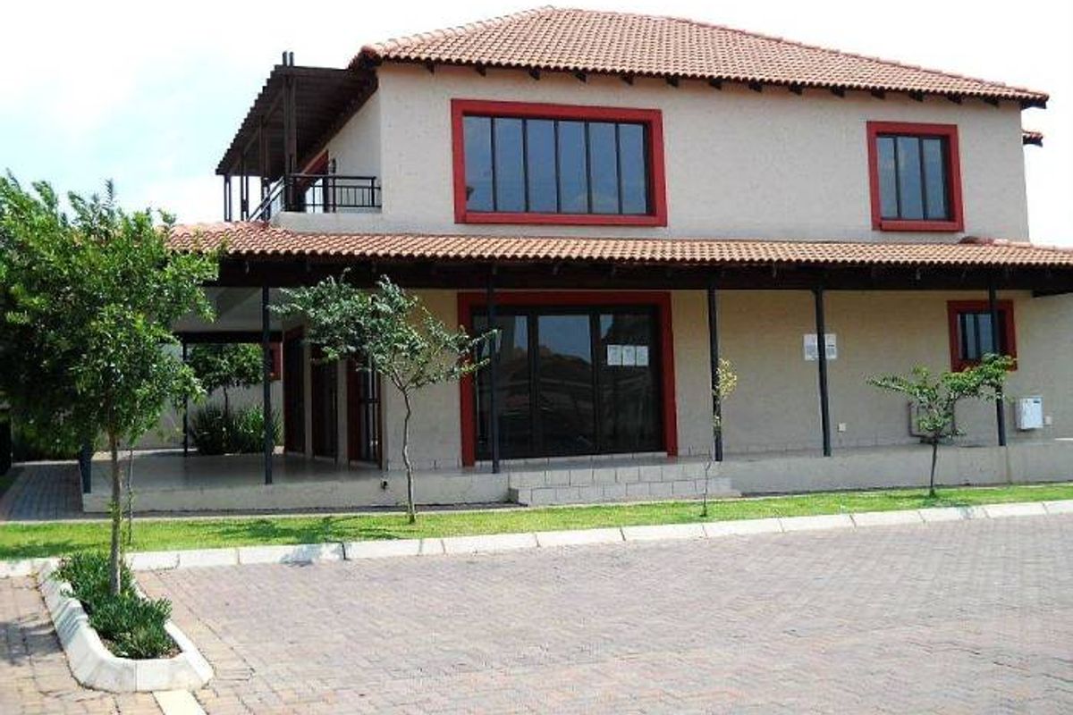 Rear view of a two-story townhouse featuring a covered patio, upper-level balcony with timber pergola, and a paved driveway area.