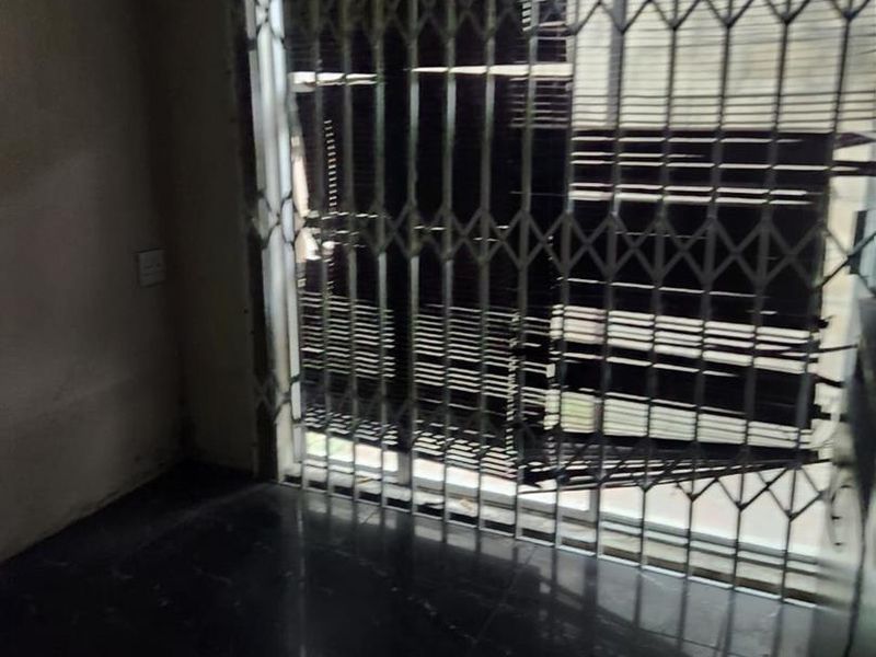 An empty living area featuring dark tiled flooring and a security gate over a sliding door, requiring cosmetic updates to improve its overall condition.
