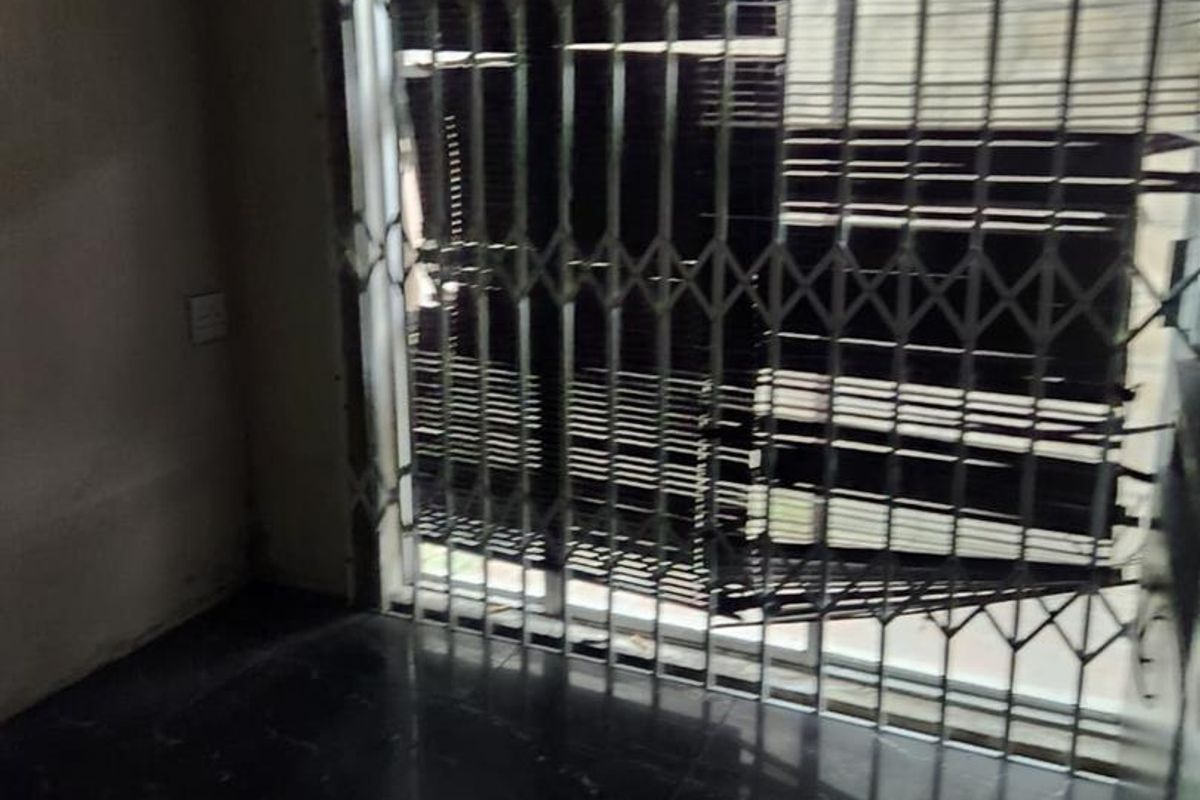 An empty living area featuring dark tiled flooring and a security gate over a sliding door, requiring cosmetic updates to improve its overall condition.