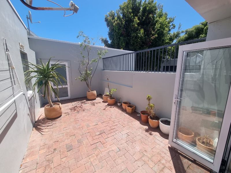 A private paved courtyard patio featuring a boundary wall with security railing and direct access to the interior via a glass sliding door.