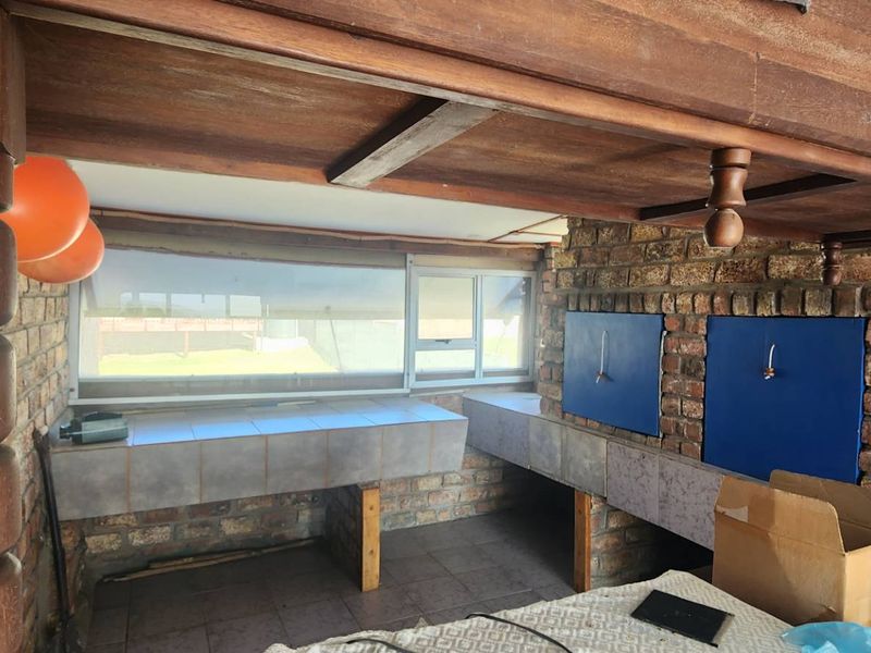 Covered outdoor patio area featuring a built-in braai, tiled prep surfaces, exposed brickwork, and timber ceiling details.