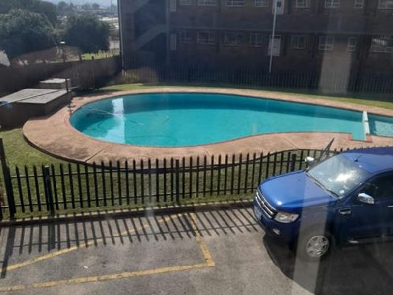 View of a communal swimming pool area with paved surround and metal fencing, situated within a townhouse complex.