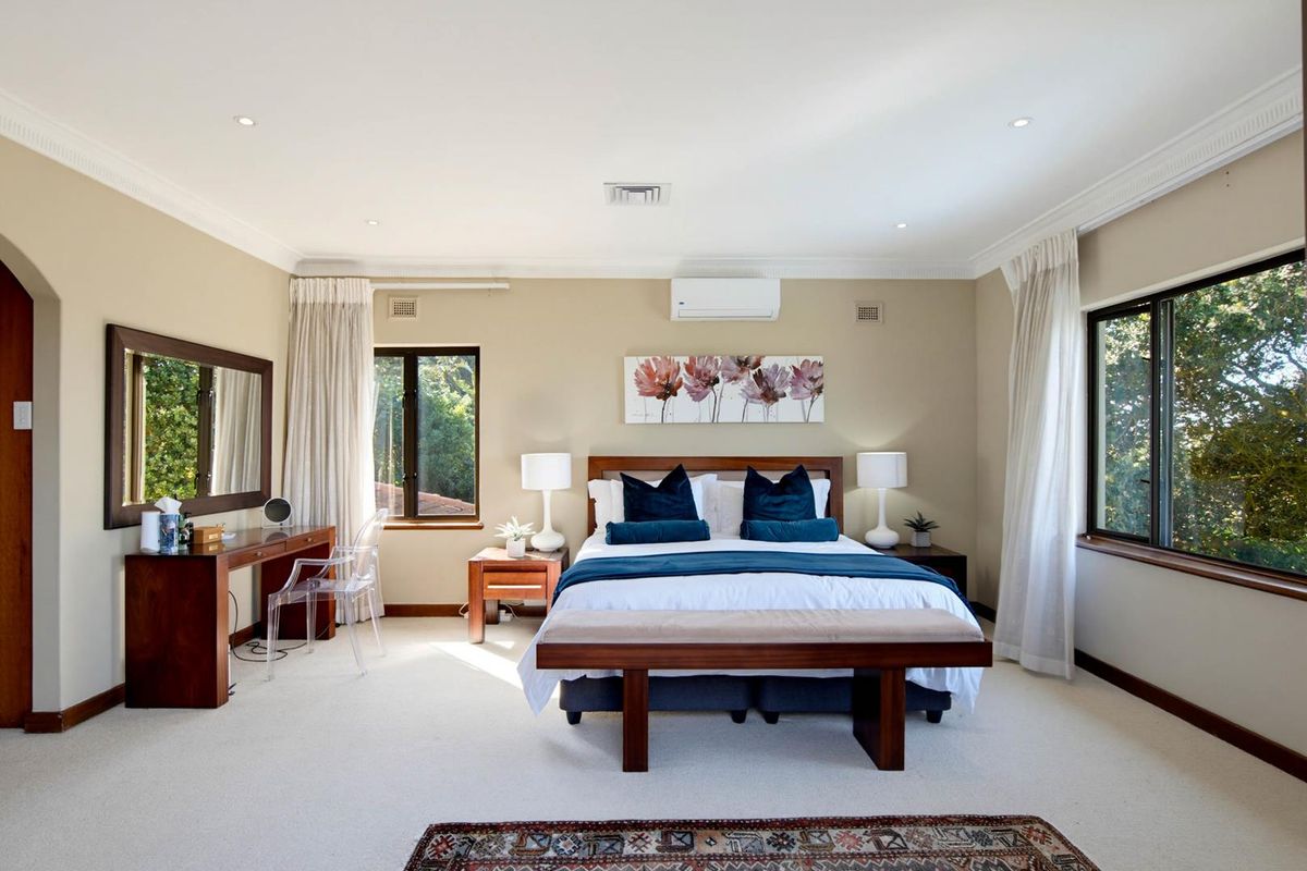Spacious bedroom featuring neutral walls, recessed downlighting, split-system air conditioning, and large windows providing natural light and garden views.