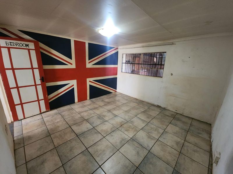 An empty bedroom featuring tiled flooring, a window with security bars, and a decorative Union Jack wall mural.