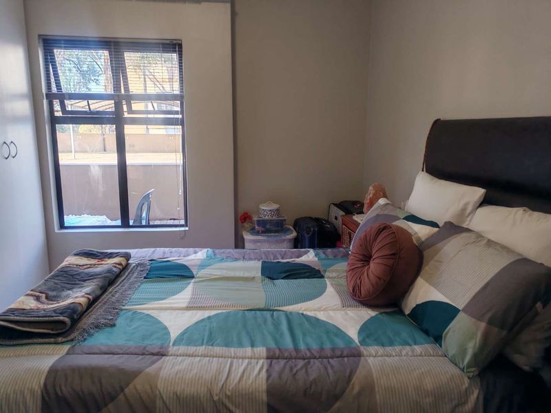 A functional bedroom featuring a window with aluminium frames and built-in cupboard storage, offering a comfortable living space.