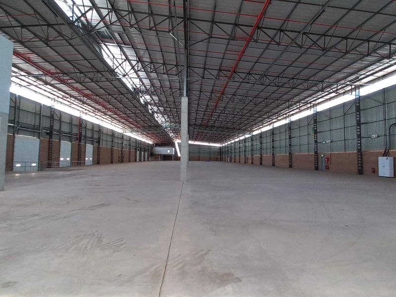 Spacious industrial warehouse featuring high ceilings with exposed steel trusses, concrete flooring, and integrated fire sprinkler systems, suitable for large-scale storage or manufacturing operations.