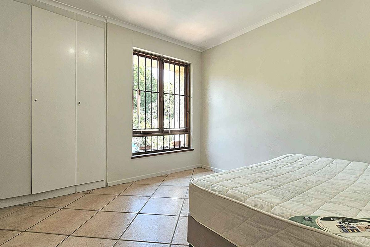 A bedroom featuring built-in cupboards, tiled flooring, and a window fitted with security bars.