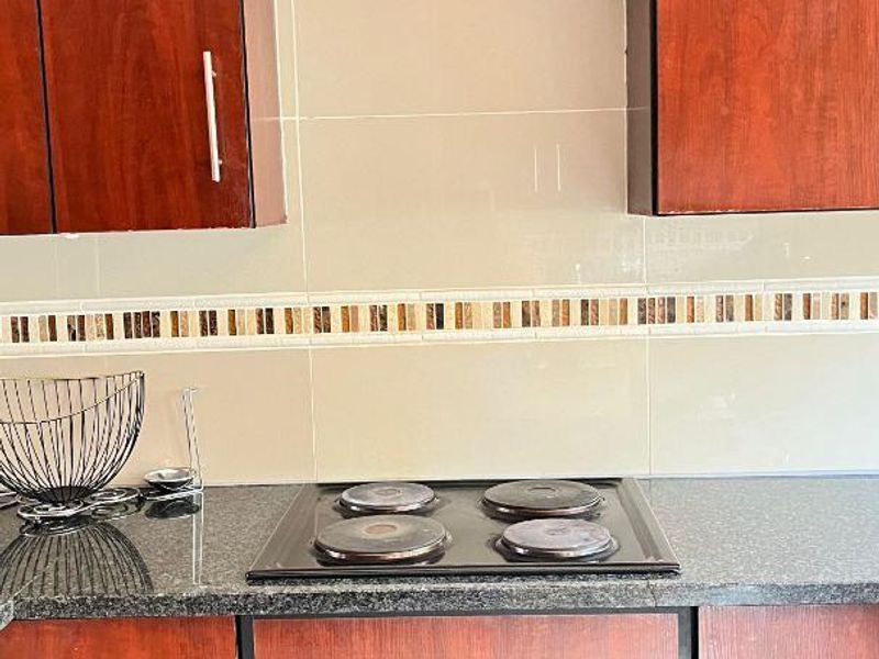 A functional kitchen area featuring dark wood cabinetry, granite countertops, and a built-in electric oven and hob with a tiled backsplash.