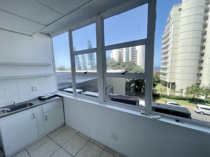 A functional scullery or utility area featuring built-in cabinetry, a stainless steel sink, and large windows offering natural light and urban views.
