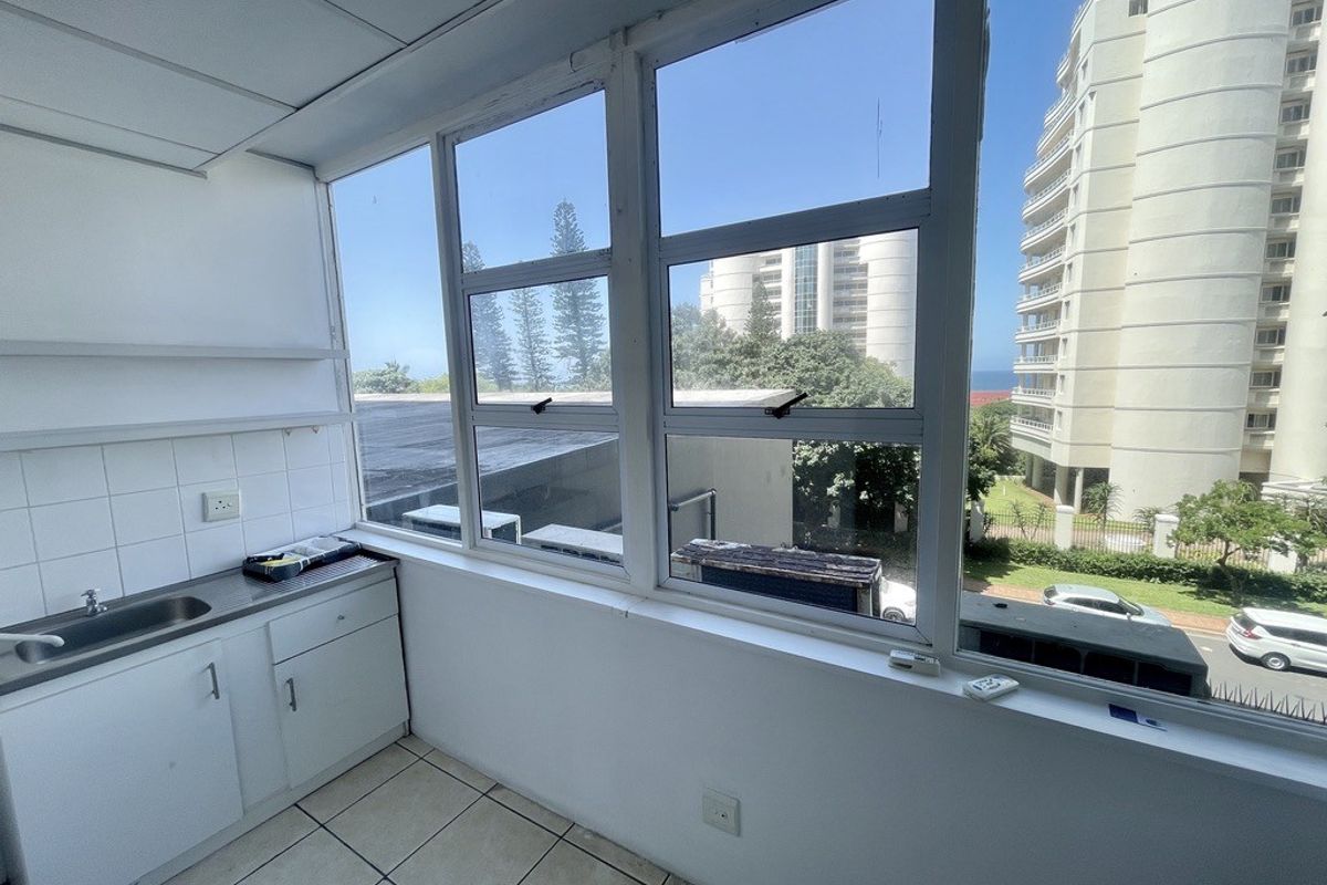 A functional scullery or utility area featuring built-in cabinetry, a stainless steel sink, and large windows offering natural light and urban views.