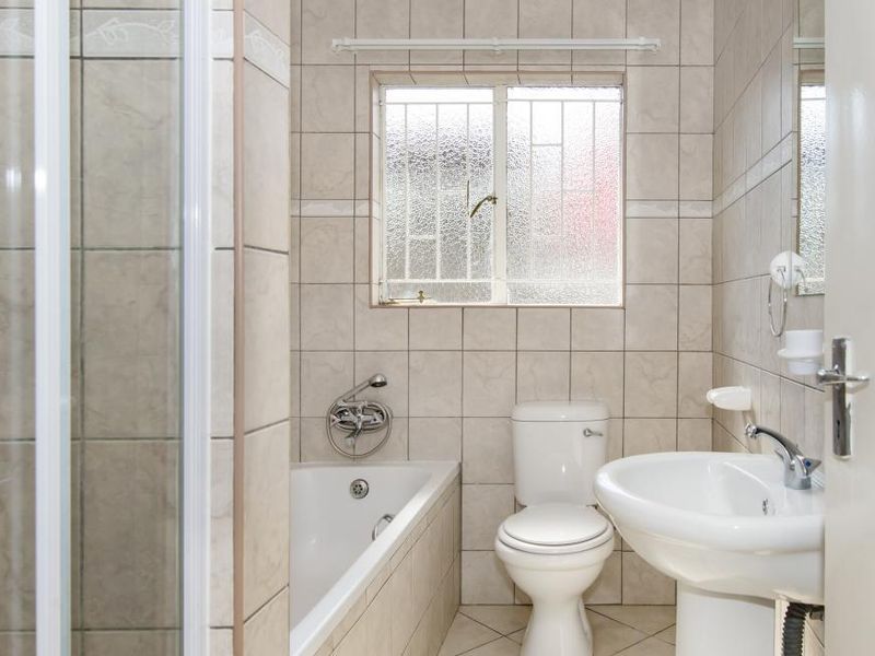 A functional bathroom featuring a shower enclosure, bathtub, pedestal basin, and toilet, finished with neutral wall and floor tiles.