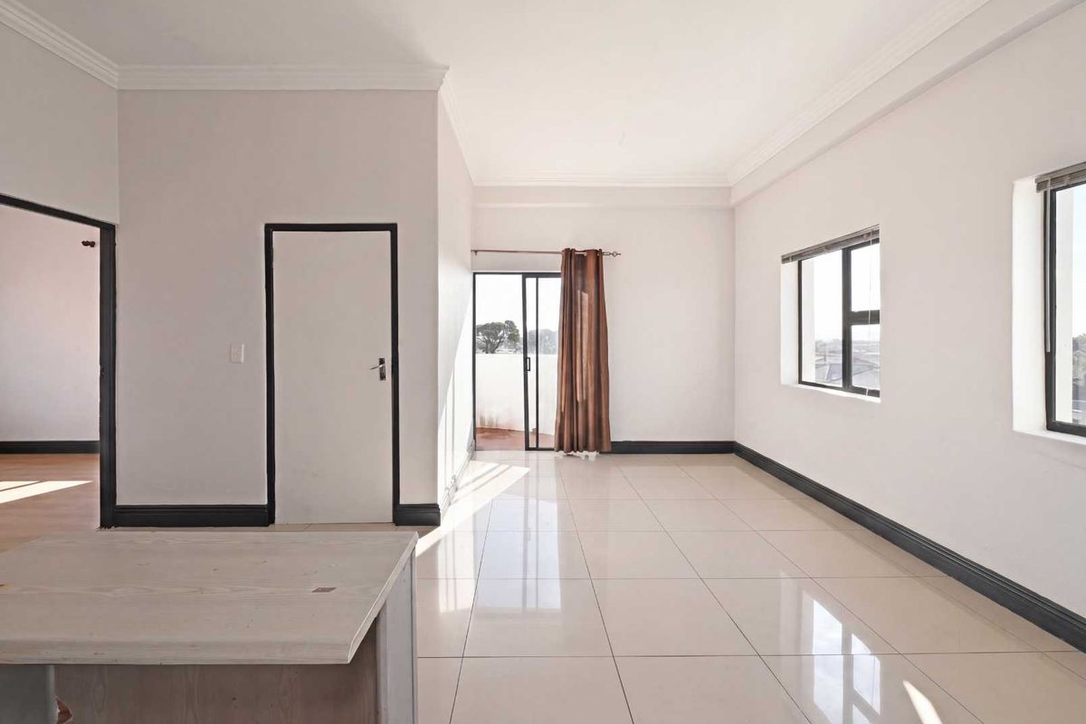A bright, open-plan living area featuring neutral tiled flooring, clean white walls, and direct access to an outdoor balcony through a sliding glass door.