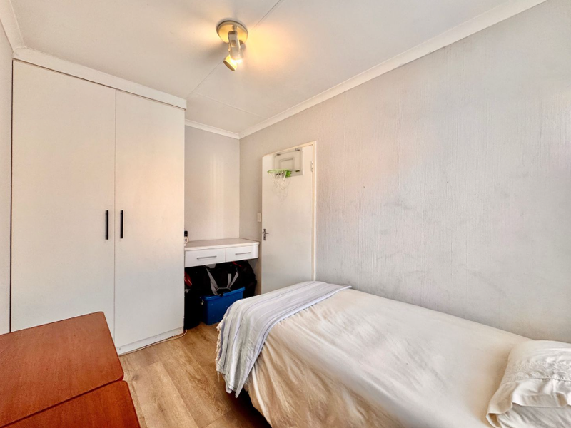 A functional bedroom featuring laminate flooring, a built-in wardrobe, and a compact built-in desk area.