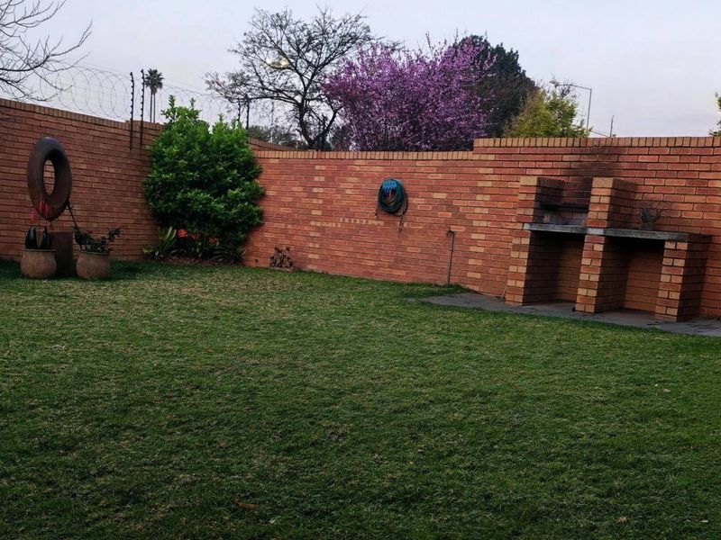 Private garden area featuring a well-maintained lawn, secure brick boundary walls with electric fencing, and a built-in brick braai facility.