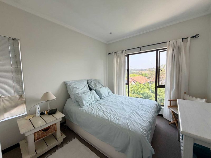 A bright bedroom featuring carpeted flooring, coved ceilings, and large windows with views, providing a comfortable and well-lit living space.