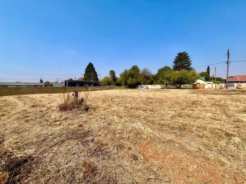 A vacant residential plot featuring dry grass, perimeter boundary walls, and clear access, suitable for new development.