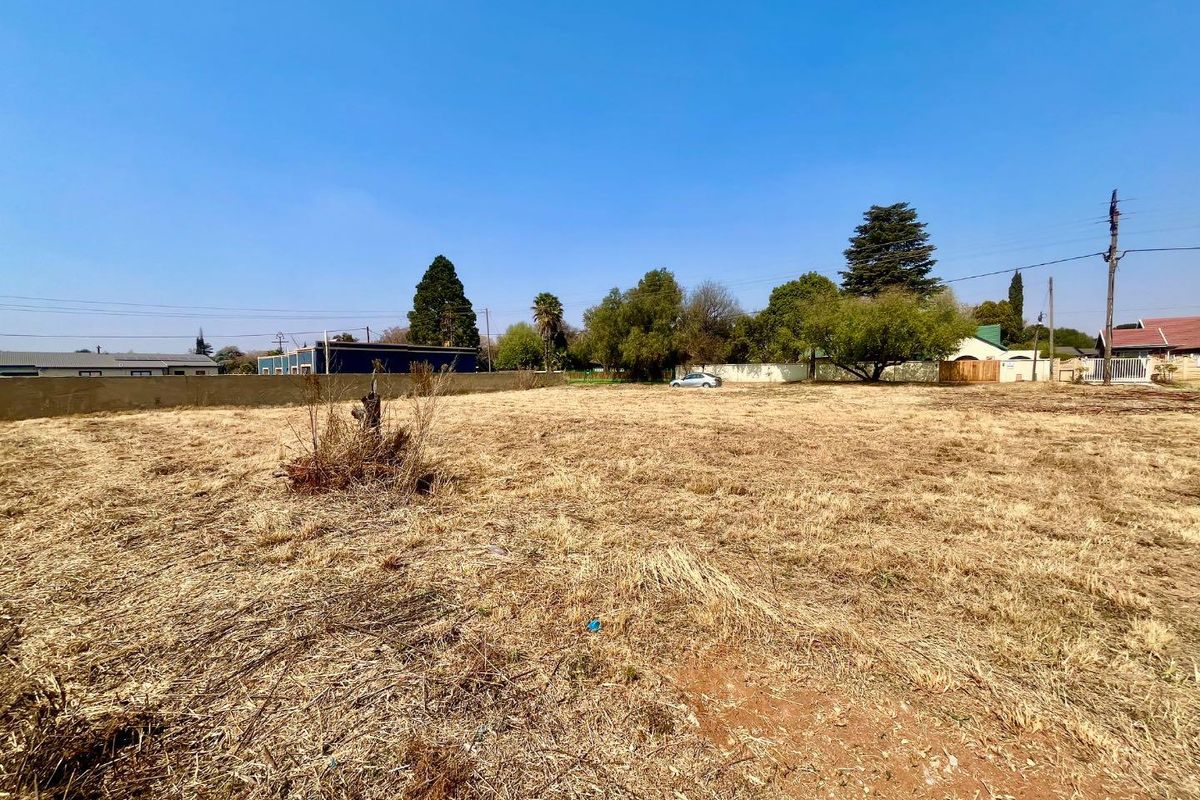 A vacant residential plot featuring dry grass, perimeter boundary walls, and clear access, suitable for new development.
