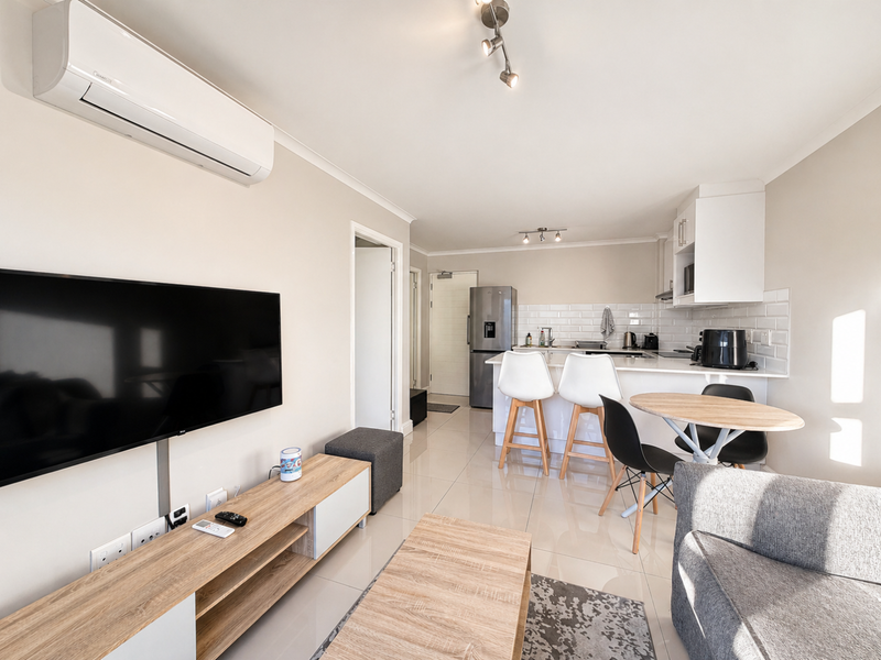 Modern open-plan living and kitchen area featuring tiled flooring, sleek cabinetry, subway tile backsplash, and a wall-mounted air conditioning unit.