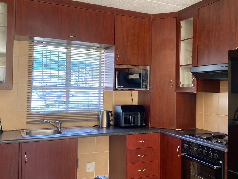 A functional kitchen featuring dark wood-finish cabinetry, tiled backsplash, integrated oven and hob, and a stainless steel sink with a window view.