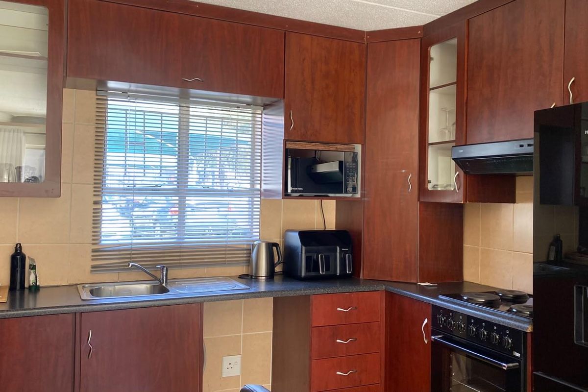 A functional kitchen featuring dark wood-finish cabinetry, tiled backsplash, integrated oven and hob, and a stainless steel sink with a window view.