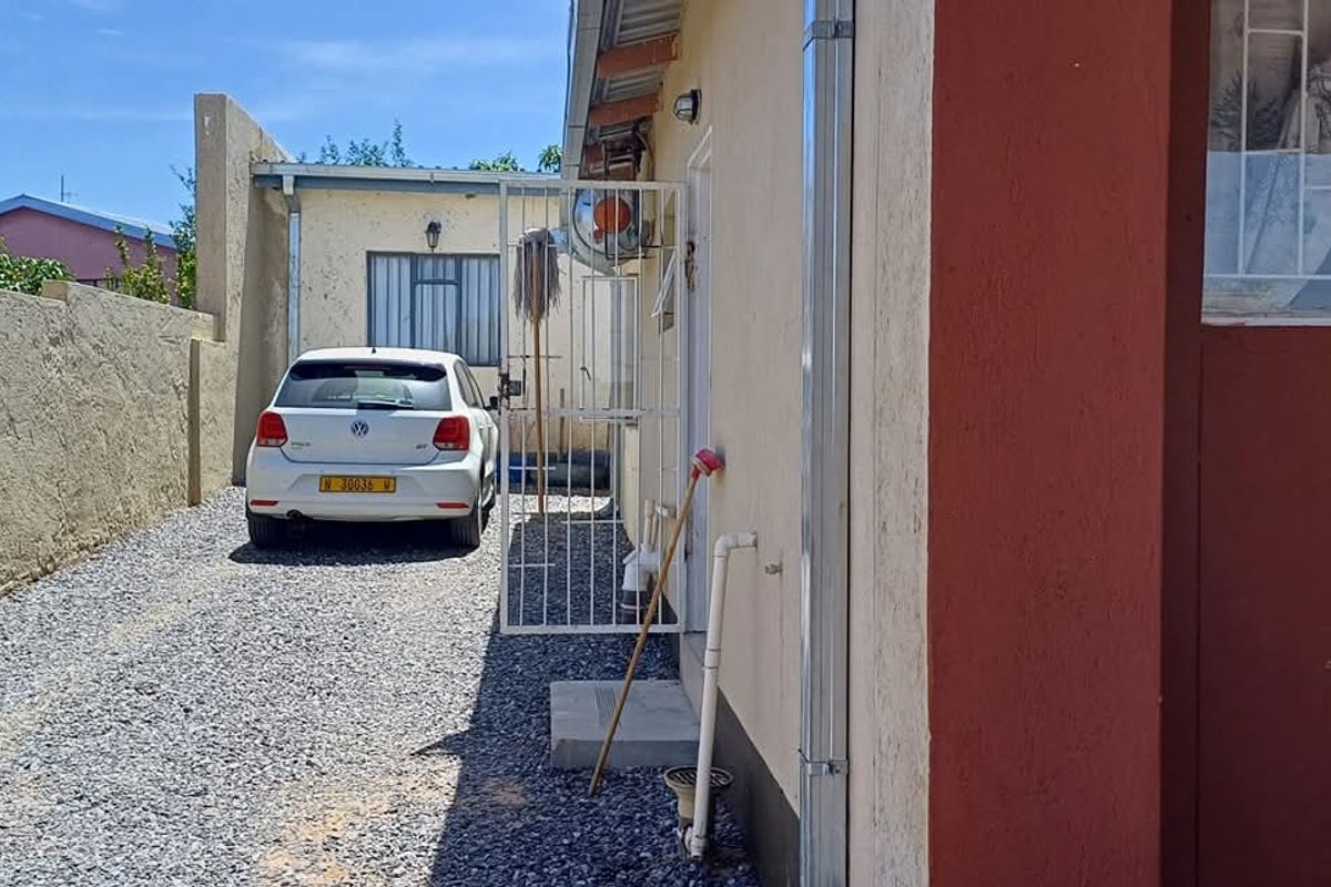 Side exterior view of the property featuring a gravel driveway, security gate, and exterior wall finishes.