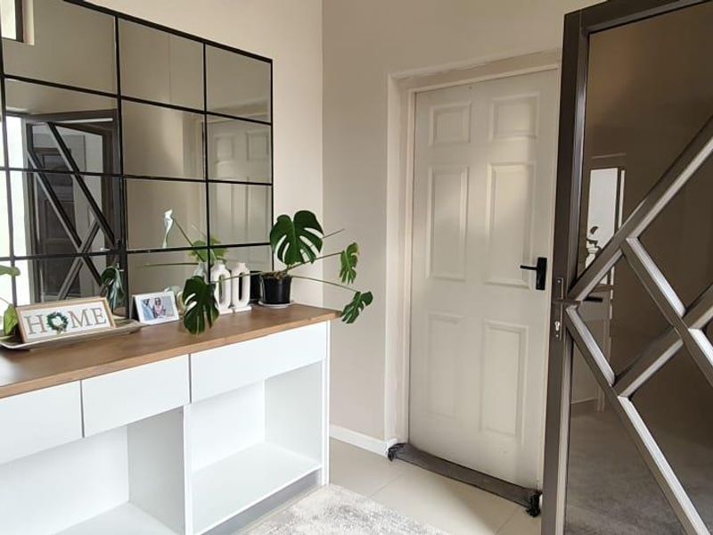 A bright and welcoming entrance hall featuring a modern built-in console table, a decorative grid-pattern mirror, and a secure entrance door.