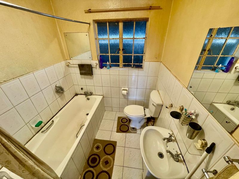 A dated bathroom featuring a standard bathtub, pedestal basin, and toilet with original tiled finishes and steel window frame.
