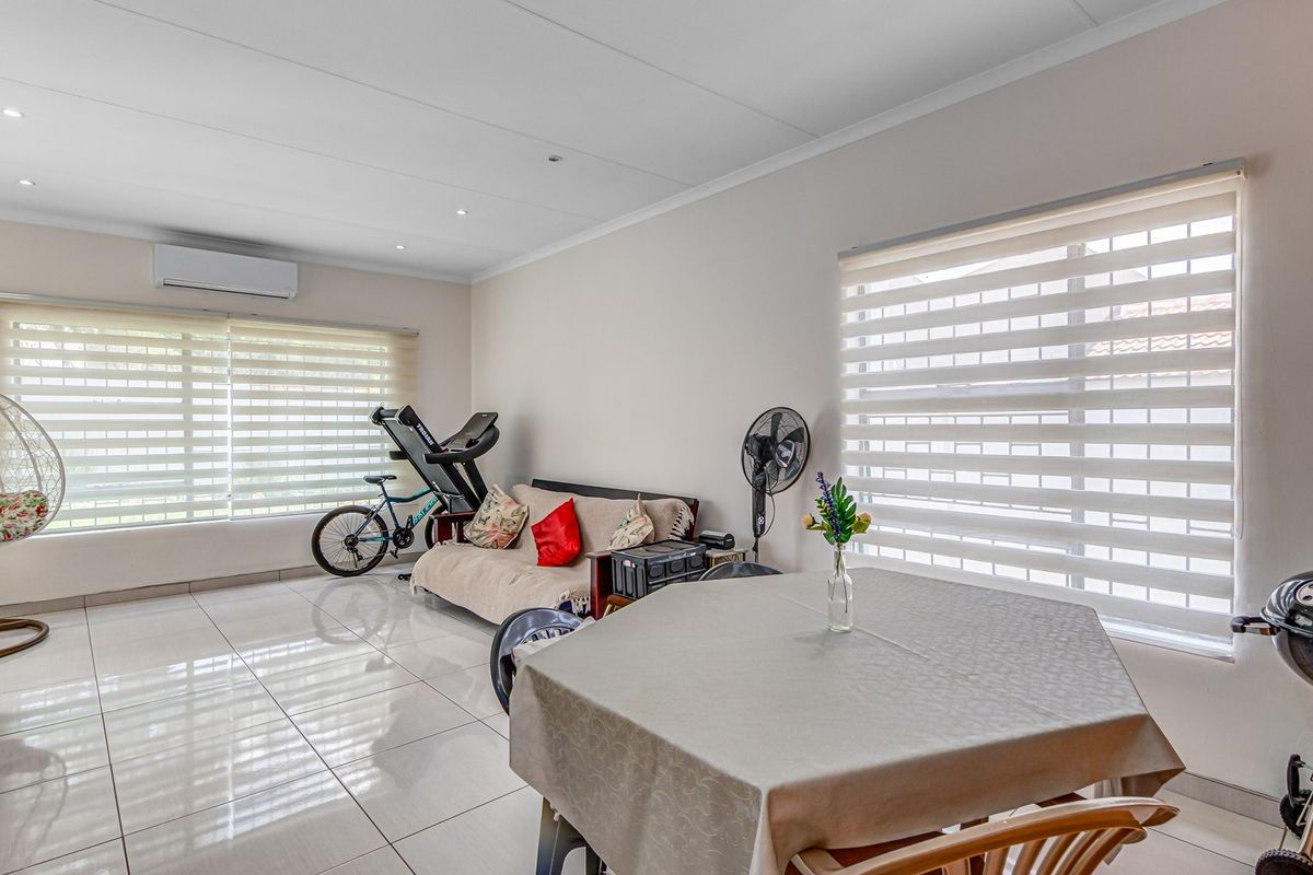 A bright, open-plan living area featuring polished floor tiles, recessed downlighting, and a wall-mounted air conditioning unit.