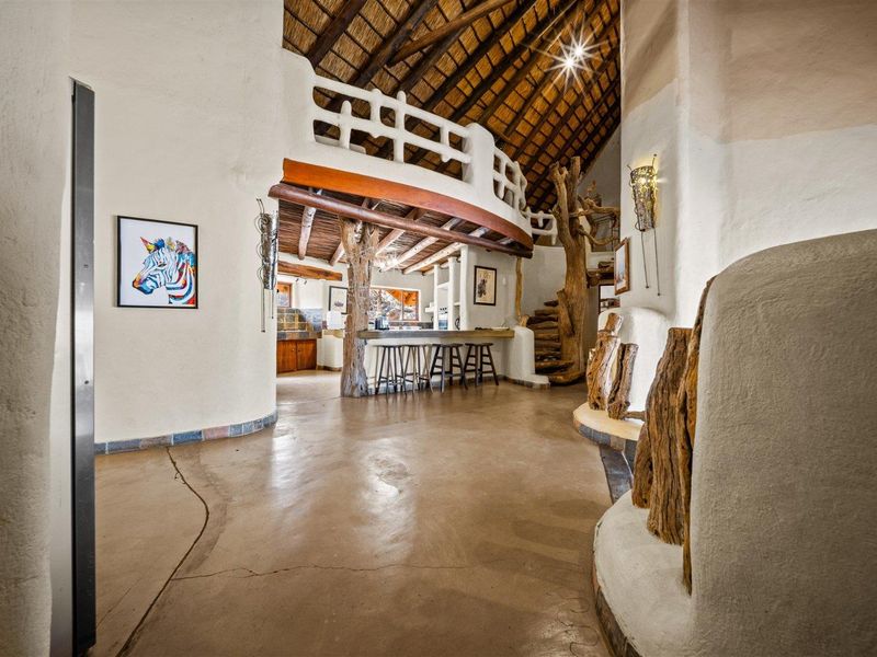 Unique open-plan living area featuring a high thatched ceiling, mezzanine level, exposed timber structural elements, and polished concrete flooring.
