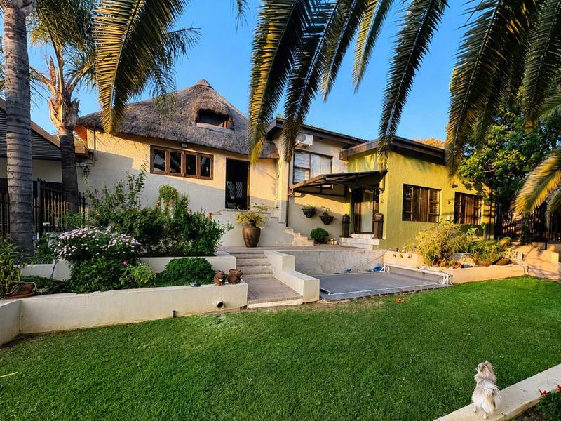 Rear view of the property featuring a thatched roof, tiered garden with retaining walls, and a paved patio area.