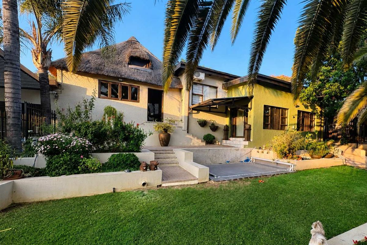Rear view of the property featuring a thatched roof, tiered garden with retaining walls, and a paved patio area.