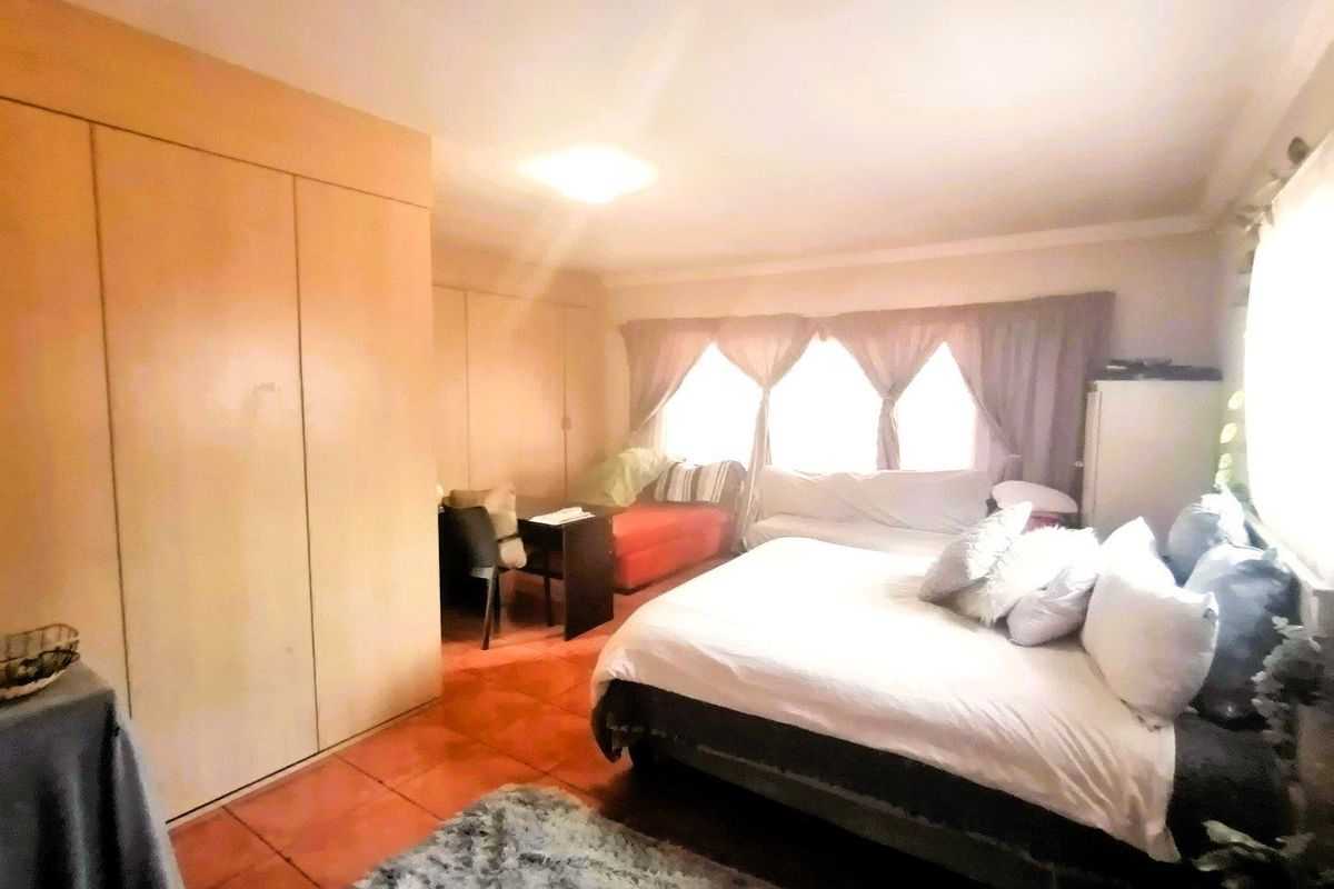 A spacious bedroom featuring extensive built-in wooden cabinetry, tiled flooring, and large windows allowing for ample natural light.