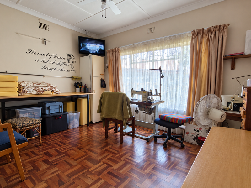 A functional bedroom featuring classic parquet flooring, a ceiling fan, and a built-in cupboard, currently utilized as a workspace.