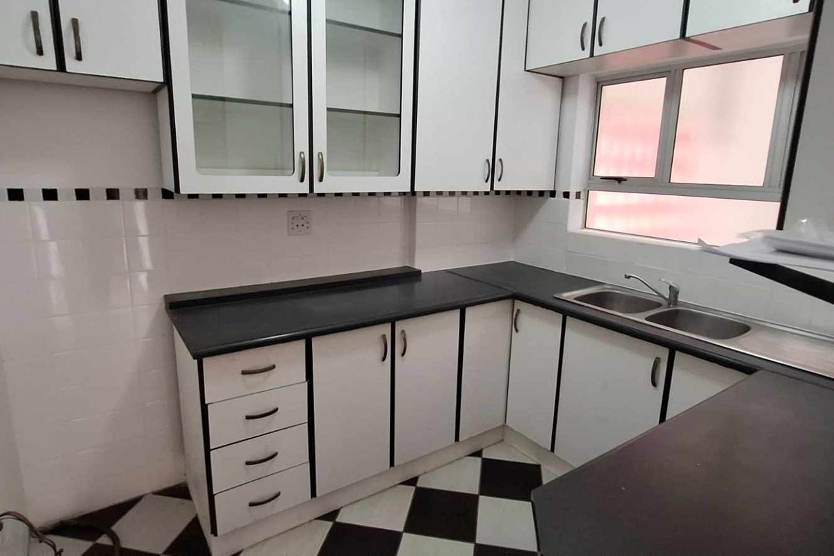 A clean, empty kitchen featuring white cabinetry with black trim, dark laminate countertops, a double stainless steel sink, and a classic checkered tile floor.