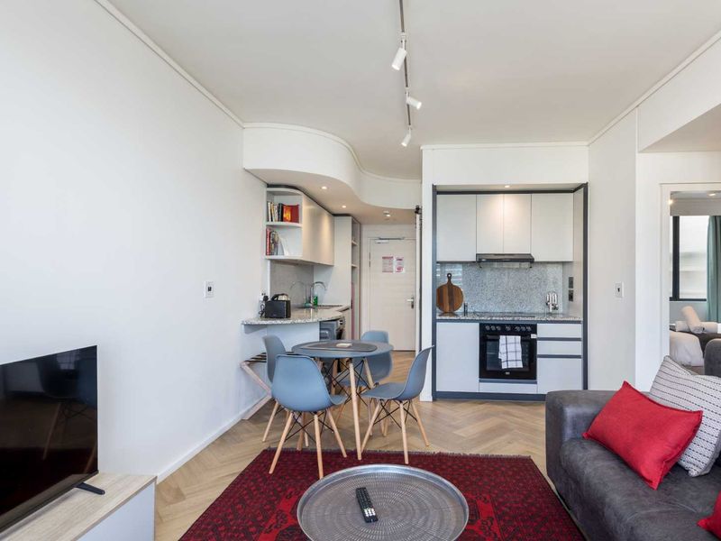 Modern open-plan living area featuring a compact kitchen with built-in cabinetry, granite countertops, integrated oven, and stylish herringbone flooring.