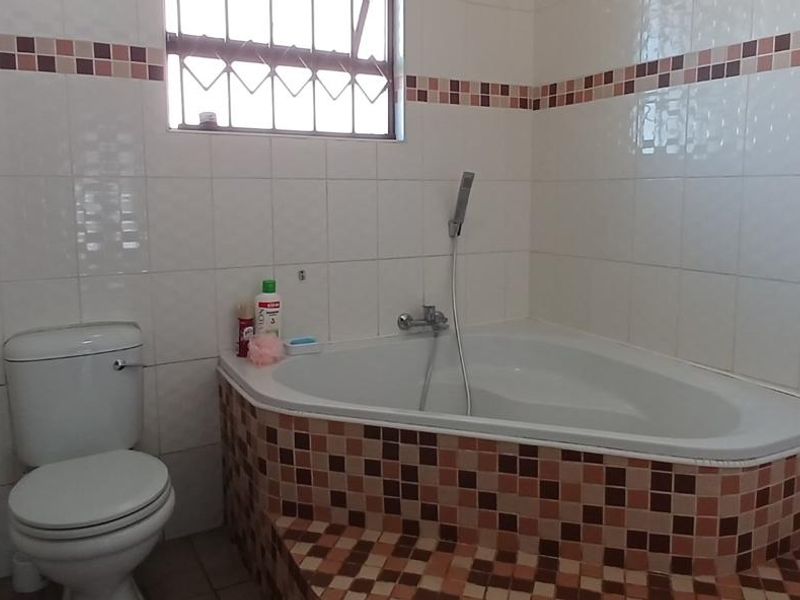 A functional bathroom featuring a corner bathtub with a handheld shower mixer, a standard toilet, and decorative tiled wall accents.