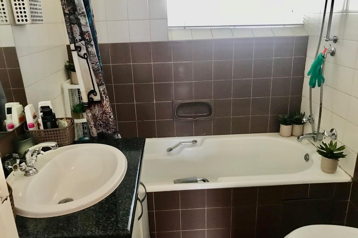 A functional bathroom featuring a built-in bathtub, vanity sink with granite countertop, and contrasting wall tiling.