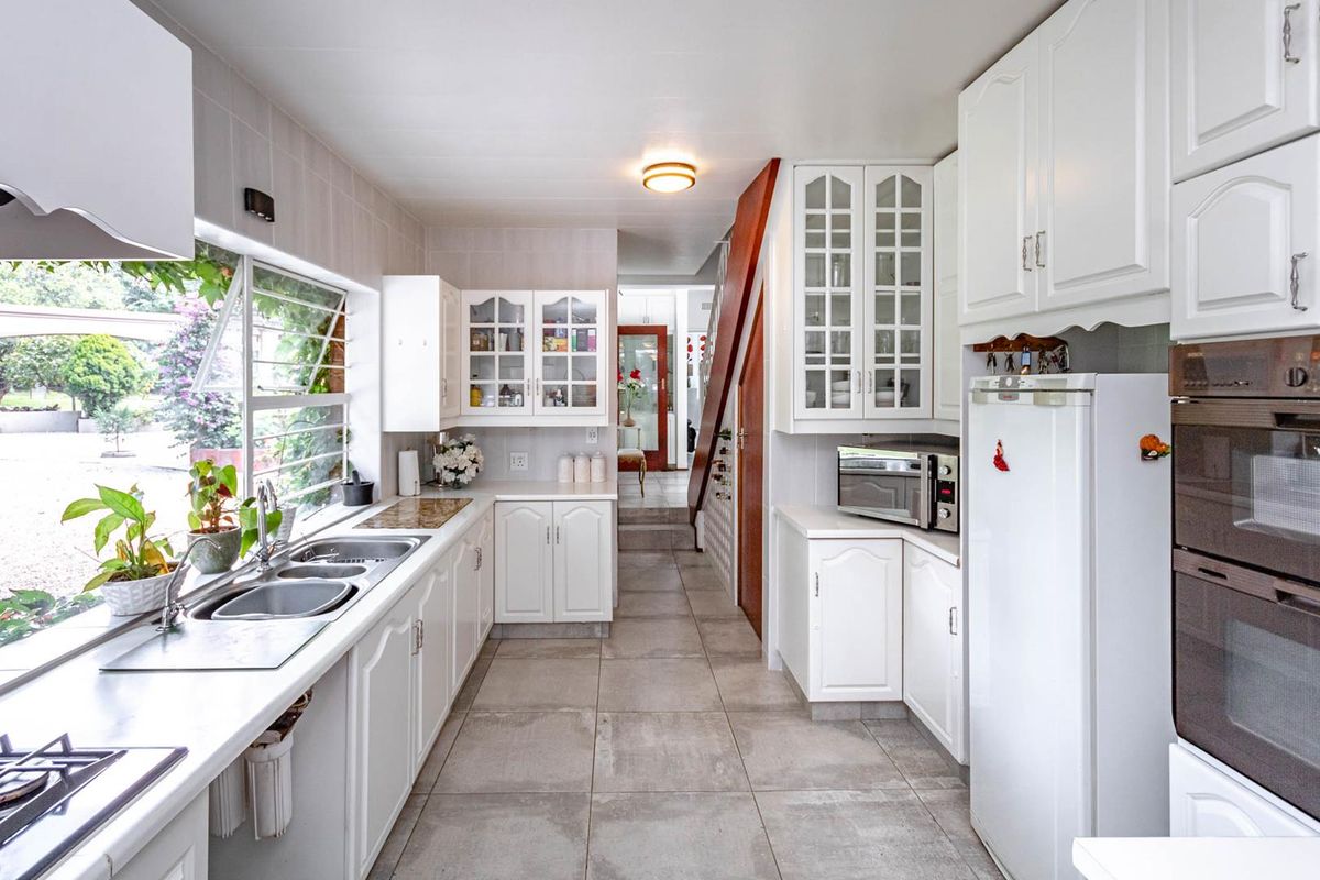 A functional kitchen featuring white cabinetry, tiled flooring, double sink, and built-in oven, with a view overlooking the garden area.