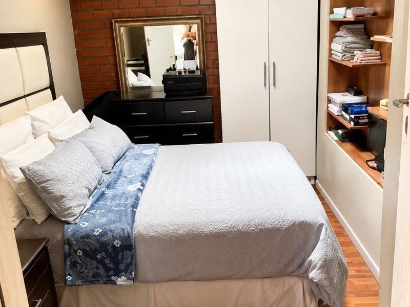 A cozy bedroom featuring an exposed brick feature wall, built-in wardrobe, integrated shelving, and warm laminate flooring.