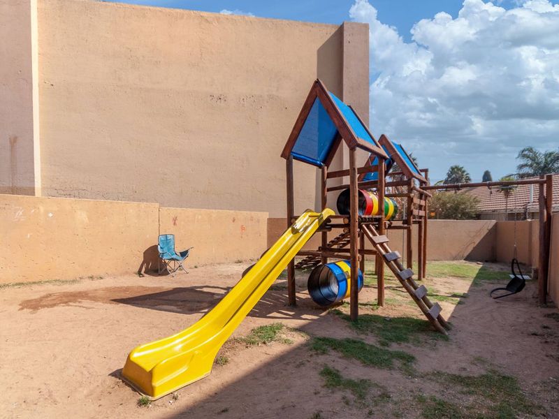 Outdoor garden area featuring a wooden playground structure with a slide, enclosed by high perimeter boundary walls.