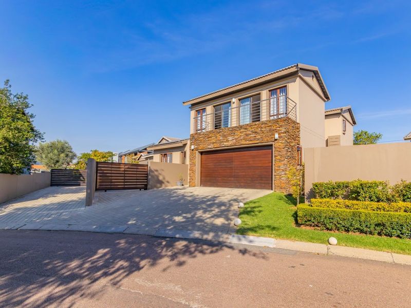 Front elevation of a modern cluster home featuring a double garage, stone-clad facade, upper-level balcony, and a paved driveway with secure gated access.