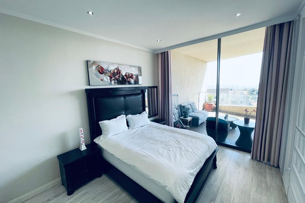 A bright bedroom featuring laminate flooring, recessed lighting, and a large sliding glass door providing direct access to a private balcony.
